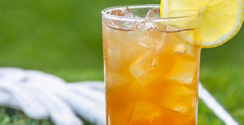 Iced tea in a tall glass with a lemon slice, set against a blurred green lawn background.