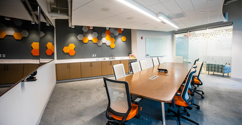 Modern conference room with a long table, orange and white chairs, and hexagonal acoustic panels on the wall, with the 'erise' logo displayed